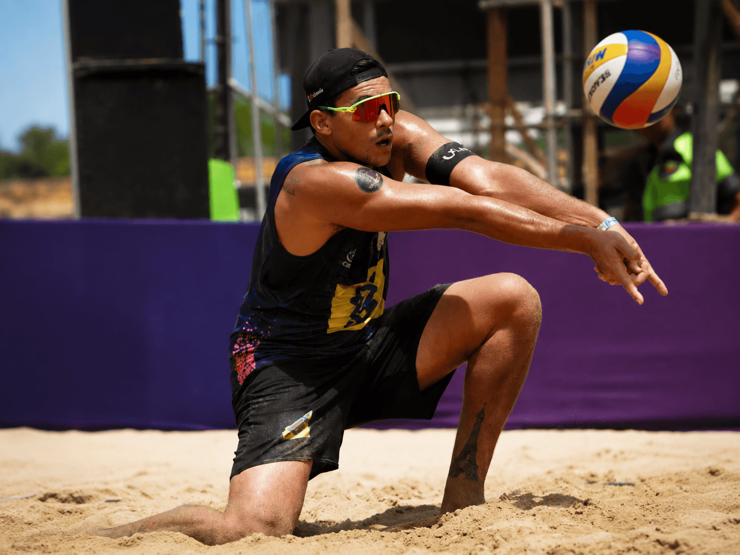 Arthur Lanci ajoelhado na areia, defendendo a bola com as duas mãos.
